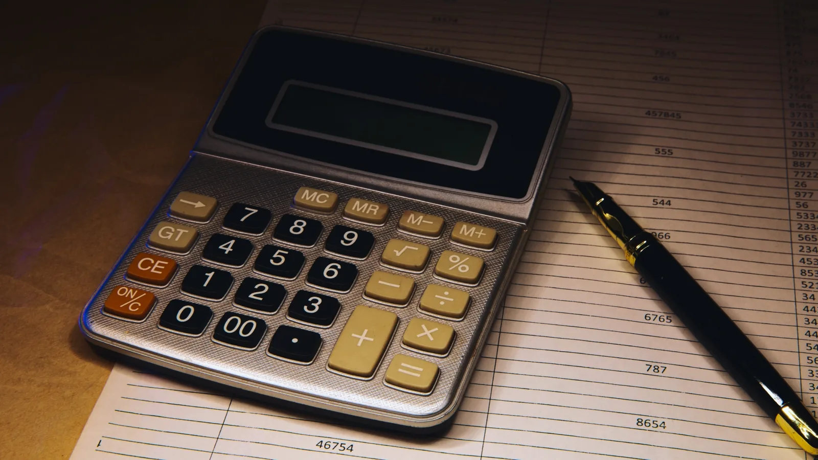 Calculadora e caneta sobre uma planilha com colunas de valores